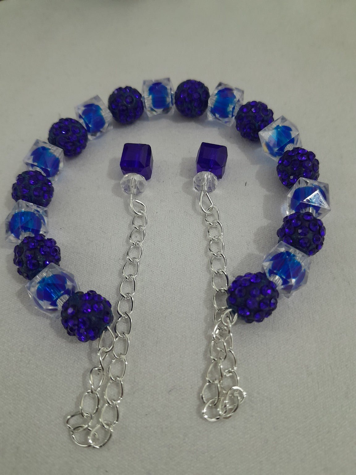 Open-ended bracelet with deep blue pavé crystal beads, clear faceted acrylic beads, and dual chain dangles with blue cube accents