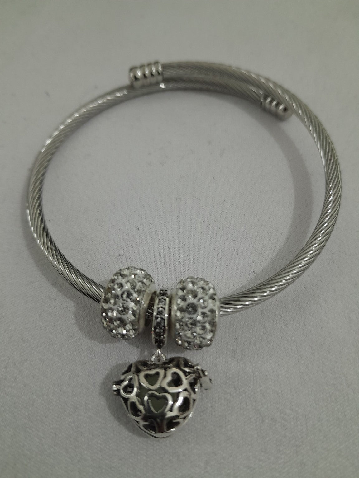 Silver-plated twisted-wire cable bangle with pavé crystal beads and filigree heart charm, flexible open-ended design for everyday wear